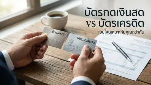 มือถือบัตรเครดิตและบัตรกดเงินสดเหนือโต๊ะทำงานไม้ เปรียบเทียบ บัตรกดเงินสด vs บัตรเครดิต พร้อมเอกสารการเงิน