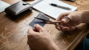 มือจับกรรไกรตัดบัตรเครดิตบนโต๊ะไม้ เพื่อแสดงขั้นตอนการปิดบัตรเครดิตอย่างปลอดภัย